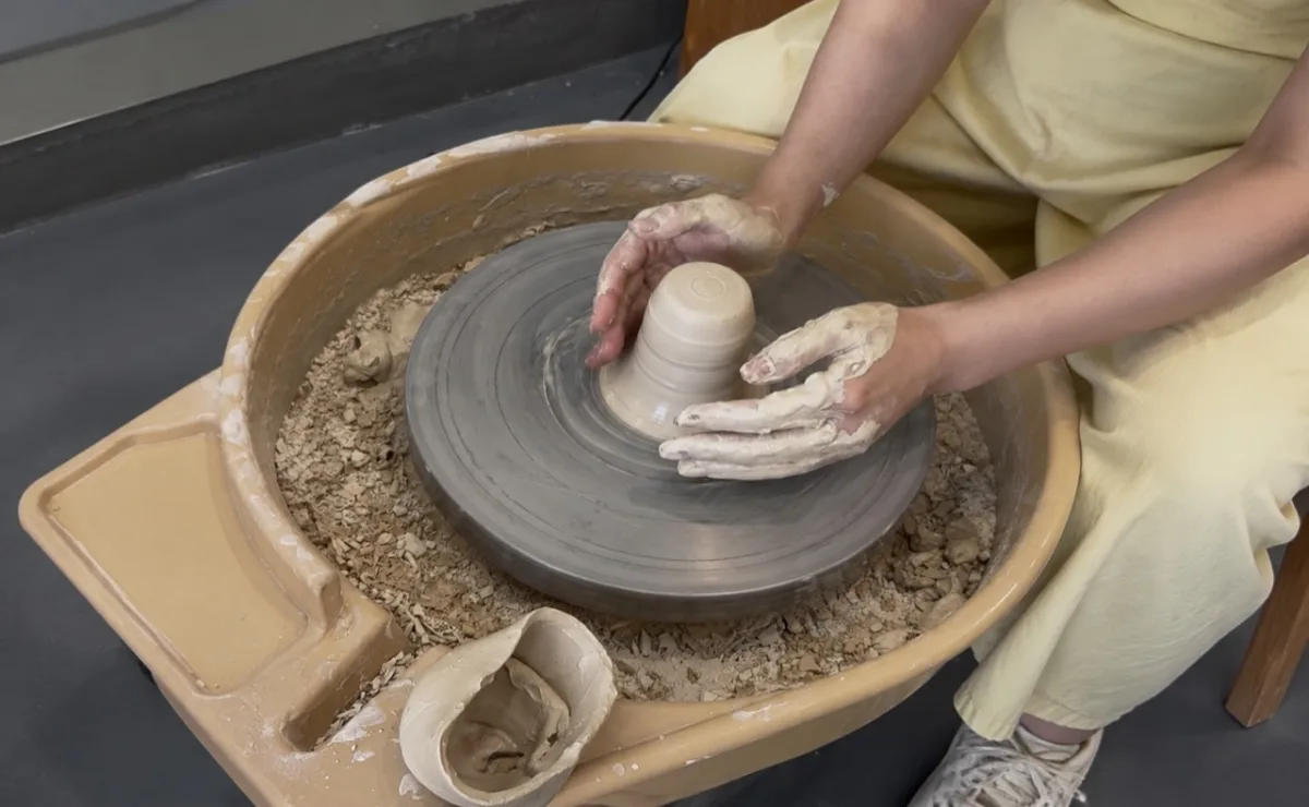 Hands shaping a ceramic cup on a pottery wheel