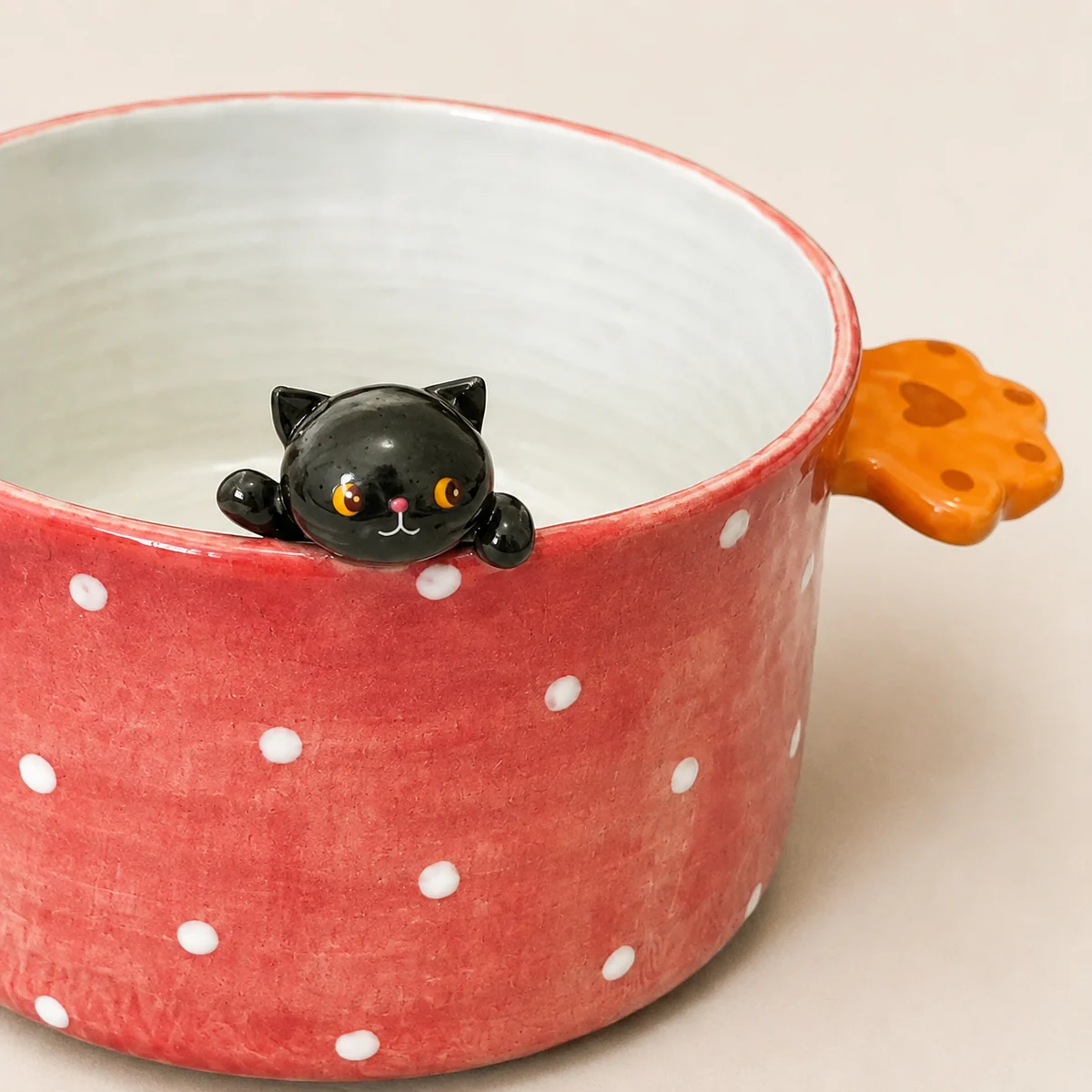 Black cat and paw handle detail on the red ceramic bowl